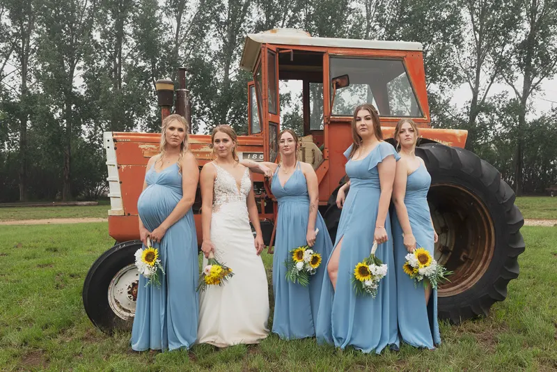 Bride and bridesmaids with sunflowers in front of an old orange tractor