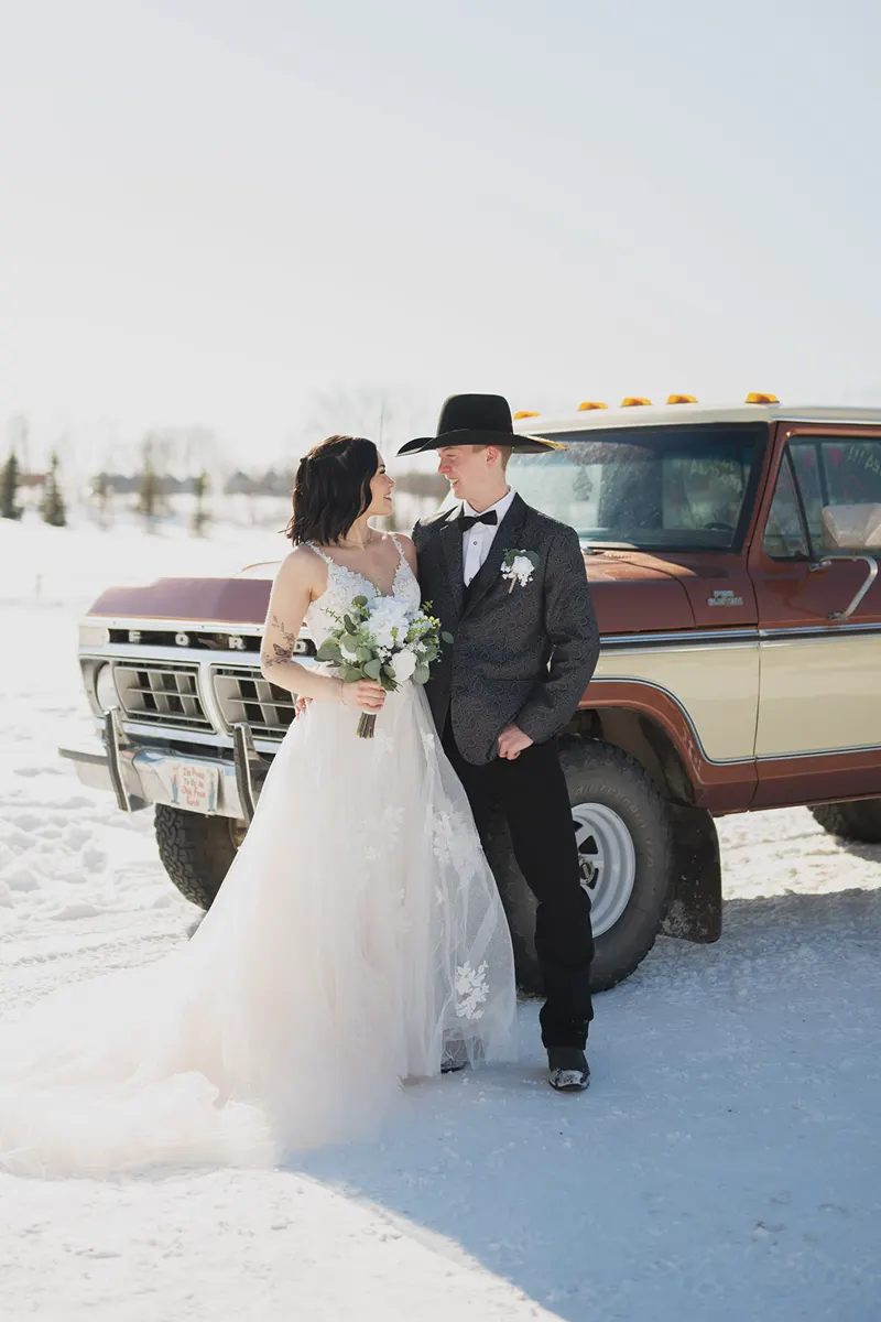 Winter bride and cowboy groom beside an old pickup in the snow